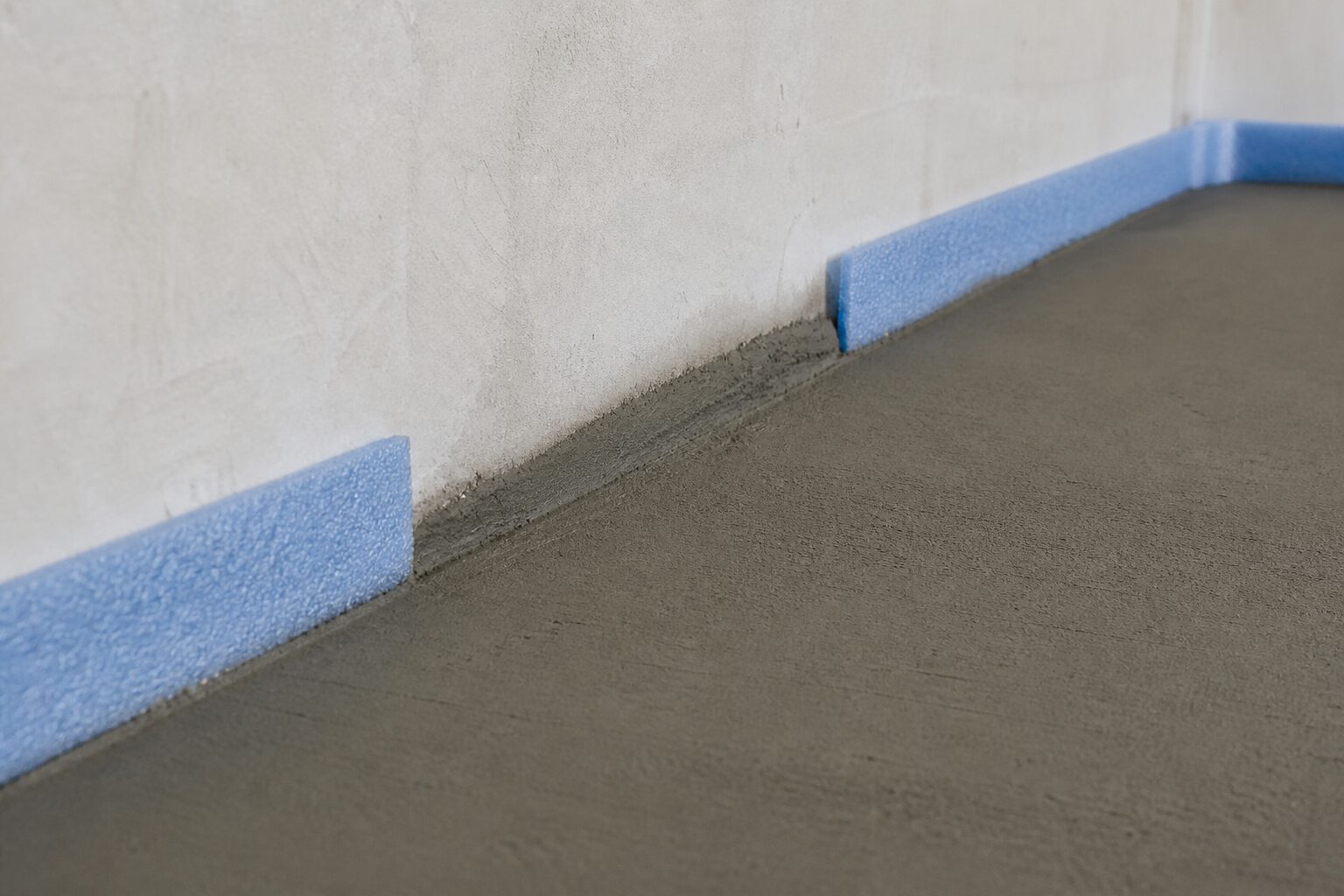 Rand eines schwimmenden Zementestrichs mit blauem Randdämmstreifen, an einer Stelle fehlt der Streifen und der Estrich stößt direkt an die Wand