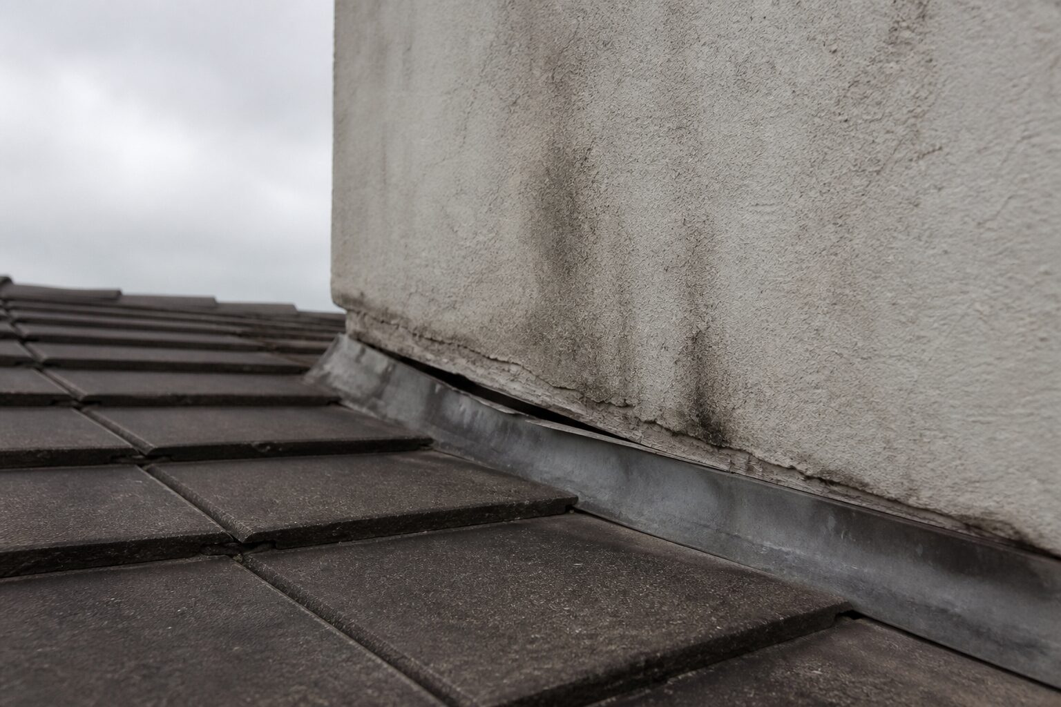 Anschluss der Dachfläche an einen verputzten Schornstein mit abgehobenem Blech und Wasserspuren