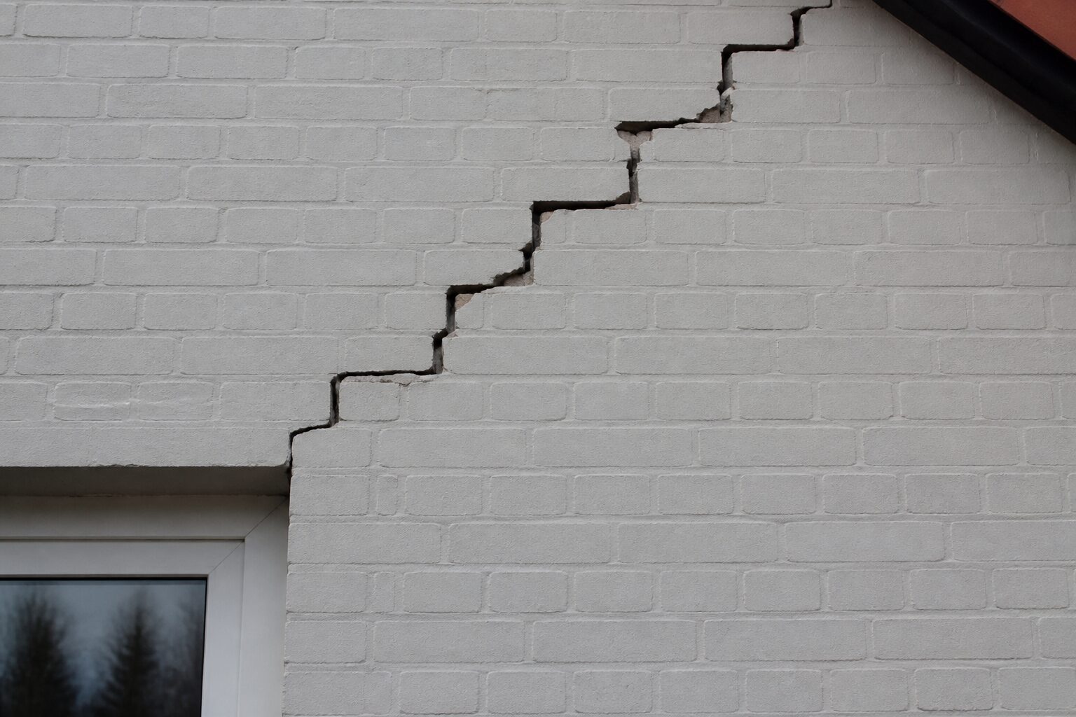 Treppenförmiger Riss im Putz einer Außenwand, von der Fensterecke diagonal nach oben verlaufend